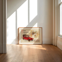 Vintage red touring car in snow print in an oak frame on a sunlit wood floor beneath tall window light