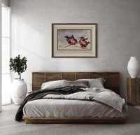 Two red robins on branch print in a dark wood frame above a rattan bed on a plaster wall