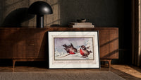 Two red robins on branch print in a black frame leaning against a walnut console in lamplight