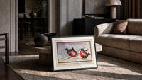 Two red robins on branch print in a slim black frame leaning on a travertine coffee table