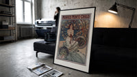 Art Nouveau woman with flowers print in a slim black frame leaning on a dark sofa in a concrete print studio