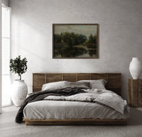 Tranquil pond with lily pads print in a dark wood frame above a rattan bed on a plaster wall