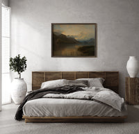 Mountain lake at sunset print in a dark wood frame above a rattan bed on a plaster wall