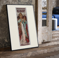Woman holding champagne glass print in a black frame leaning beside a vintage door on parquet