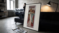 Woman holding champagne glass print in a slim black frame leaning on a dark sofa in a concrete print studio