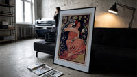 Woman with flowing dark hair smoking print in a slim black frame leaning on a dark sofa in a concrete print studio