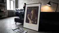 Woman with flowing hair smoking print in a slim black frame leaning on a dark sofa in a concrete print studio