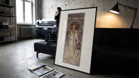 Art Nouveau woman with flowers print in a slim black frame leaning on a dark sofa in a concrete print studio