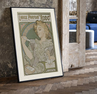 Art Nouveau woman spraying perfume print in a black frame leaning beside a vintage door on parquet