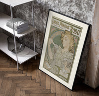 Art Nouveau woman spraying perfume poster in a black frame leaning beside a shelf in a raw-plaster loft
