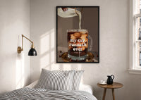 My Cup Runneth Over Coffee print in a black frame above a bed with striped linens, a brass wall lamp and a sunlit window