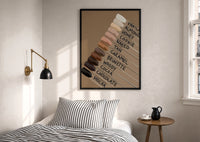 Nail Swatches in Brown Tones print in a black frame above a bed with striped linens, a brass wall lamp and a sunlit window