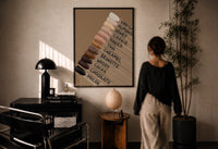 Nail Swatches in Brown Tones print in a black frame on a sunlit plaster wall, a woman looking on beside a mushroom lamp