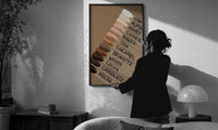 Nail Swatches in Brown Tones print in a slim black frame being hung on a sunlit wall in a monochrome room