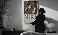 Nike Air Force 1 Low on Brown print in a slim black frame being hung on a sunlit wall in a monochrome room