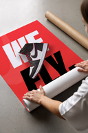 Person unrolling a red poster featuring Nike Air Jordan 1 We Fly sneaker with bold white and black text design
