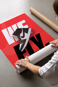 Hands unrolling a red Air Jordan 1 We Fly poster with bold white and black sneaker text design