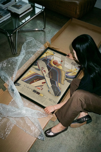 Woman unpacking a framed colourful Air Max 97 Wotherspoon sneaker poster from a cardboard box