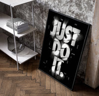 Just Do It typography design poster in a black frame leaning beside a shelf in a raw-plaster loft