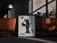 Black-framed KAWS Companion figure standing print on a moody console with designer coffee-table books