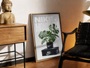 Brass-framed Monstera plant in Nike pot print leaning in a warm styled corner by a sculpture