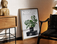 Brass-framed Monstera plant in Nike pot print leaning in a warm styled corner by a sculpture