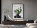 Monstera plant in Nike pot poster framed above a wood console in a concrete-wall living room