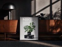 Black-framed Monstera plant in Nike pot print on a moody console with designer coffee-table books