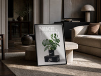 Monstera plant in Nike pot print in a black frame leaning on a travertine table in a sunlit lounge