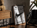 Walnut-framed Nike Swoosh logo design study print leaning against a sunlit rustic brick wall