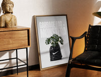 Brass-framed Monstera plant in Nike garbage bag print leaning in a warm styled corner by a sculpture