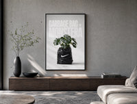 Monstera plant in Nike garbage bag poster framed above a wood console in a concrete-wall living room