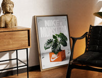 Brass-framed Monstera plant in Nike shoe box print leaning in a warm styled corner by a sculpture