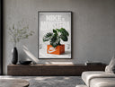 Monstera plant in Nike shoe box poster framed above a wood console in a concrete-wall living room