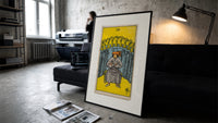 Seated man before nine golden cups print in a slim black frame leaning on a dark sofa in a concrete print studio