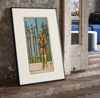 Man holding wooden staff among wands print in a black frame leaning beside a vintage door on parquet
