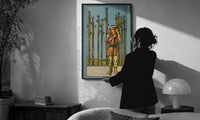 Nine of Wands print in a slim black frame being hung on a sunlit wall in a monochrome room