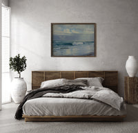 Ocean waves crashing on beach print in a dark wood frame above a rattan bed on a plaster wall