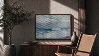 Ocean waves crashing on beach print in a wood frame above a fluted sideboard beside an olive tree