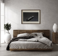 advertising blimp airship print in a dark wood frame above a rattan bed on a plaster wall