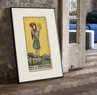 Youth holding pentacle coin print in a black frame leaning beside a vintage door on parquet