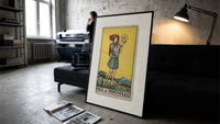 Youth holding pentacle coin print in a slim black frame leaning on a dark sofa in a concrete print studio