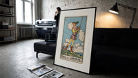 Young figure holding upraised sword print in a slim black frame leaning on a dark sofa in a concrete print studio