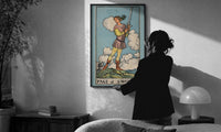 Page of Swords print in a slim black frame being hung on a sunlit wall in a monochrome room