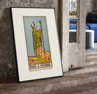 Page of Wands tarot figure print in a black frame leaning beside a vintage door on parquet