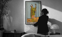 Page of Wands print in a slim black frame being hung on a sunlit wall in a monochrome room