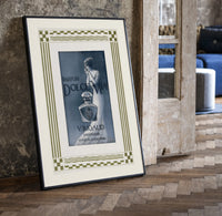 Elegant woman with perfume bottle print in a black frame leaning beside a vintage door on parquet