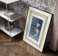 Elegant woman with perfume bottle poster in a black frame leaning beside a shelf in a raw-plaster loft
