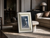 Elegant woman with perfume bottle print in a black frame leaning on a travertine table in a sunlit lounge
