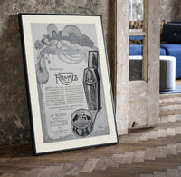 Reclining Egyptian woman perfume advertisement print in a black frame leaning beside a vintage door on parquet